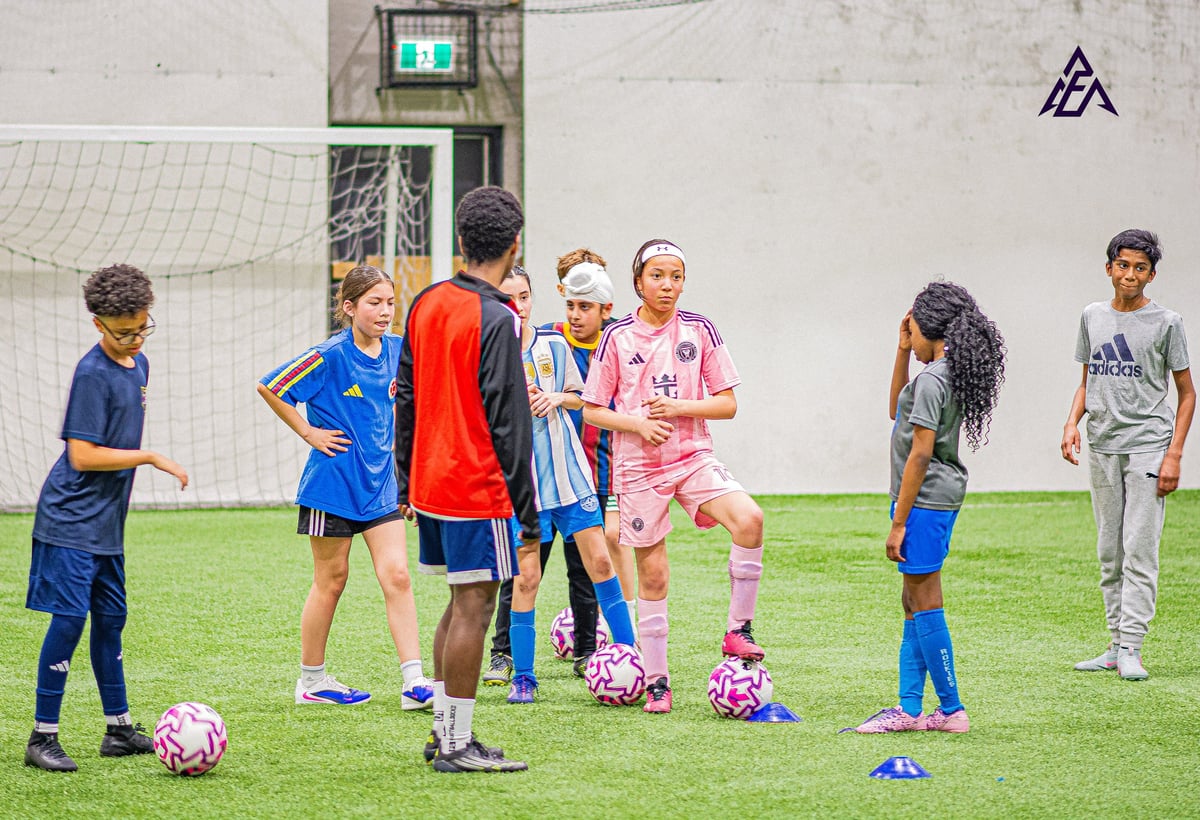 Group of young children gathered on a grass soccer field during training or practice session indoors
