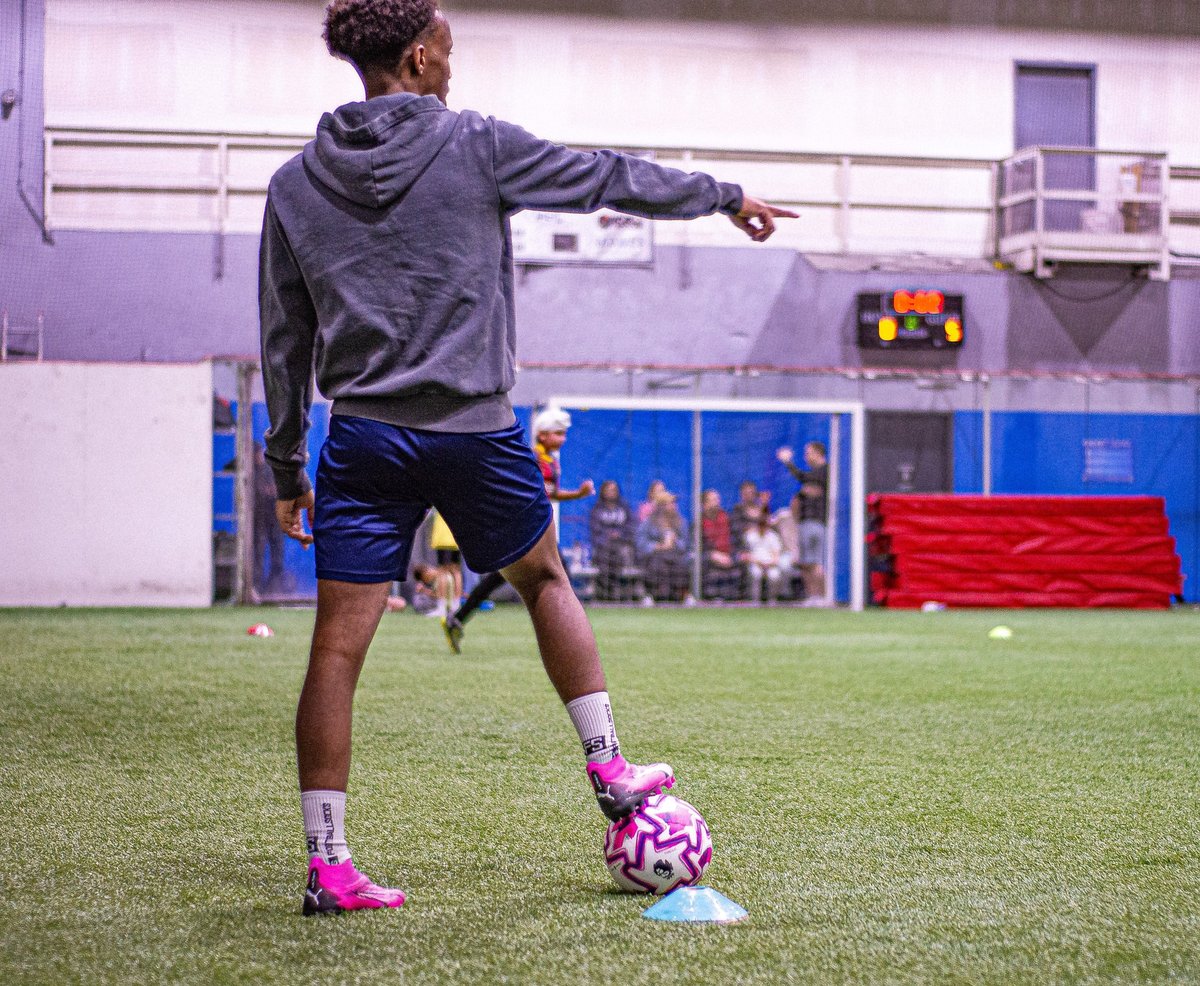 Young soccer player in blue shorts and gray hoodie controlling the ball with their foot during indoor training session