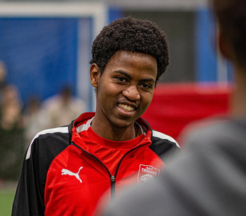 Young male athlete smiling while wearing a red and black Puma sports jacket at an indoor sports facility